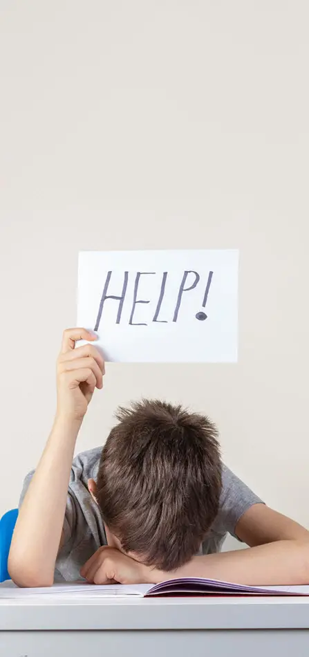 A child sitting down on a chair, head down on the table, with a sign in his hand that says "Help!" | Autism Test