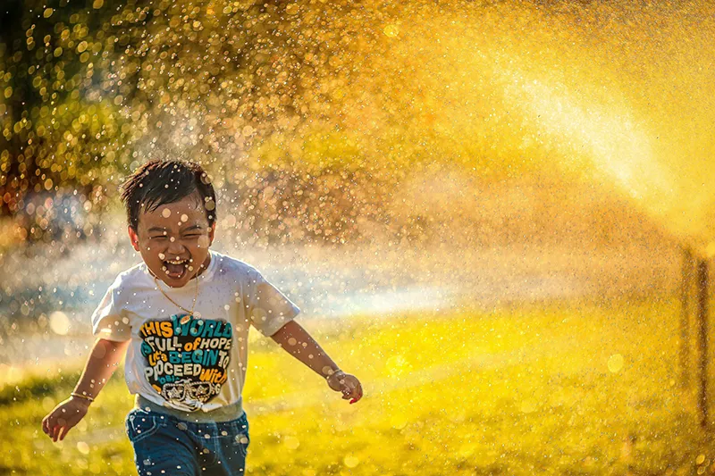 A child running on the grass outside, running through the water sprinkler and getting wet, while joyful | Autism Test