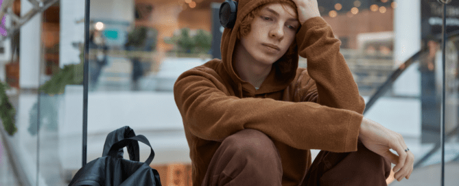 Upset teenage boy in headphones sitting nearby moving staircase | Typical teenager behaviour